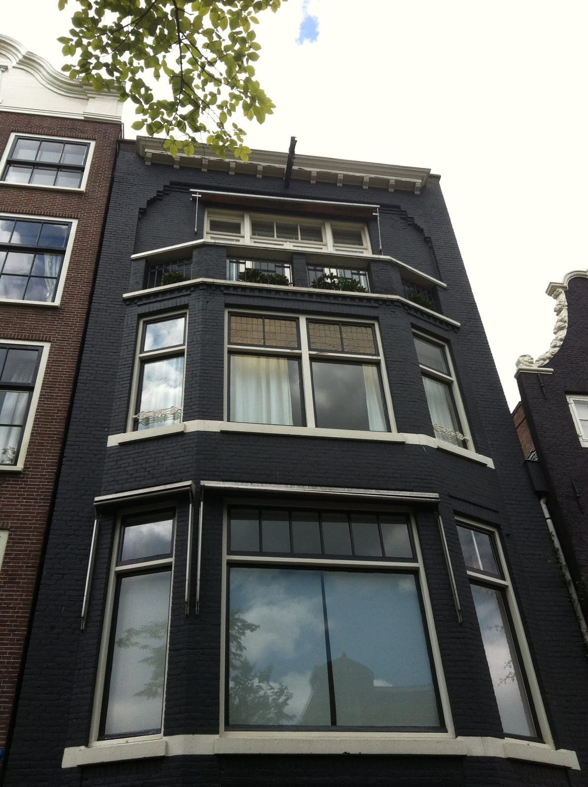 Donker geschilderd grachtenpand met witte kozijnen in Amsterdam