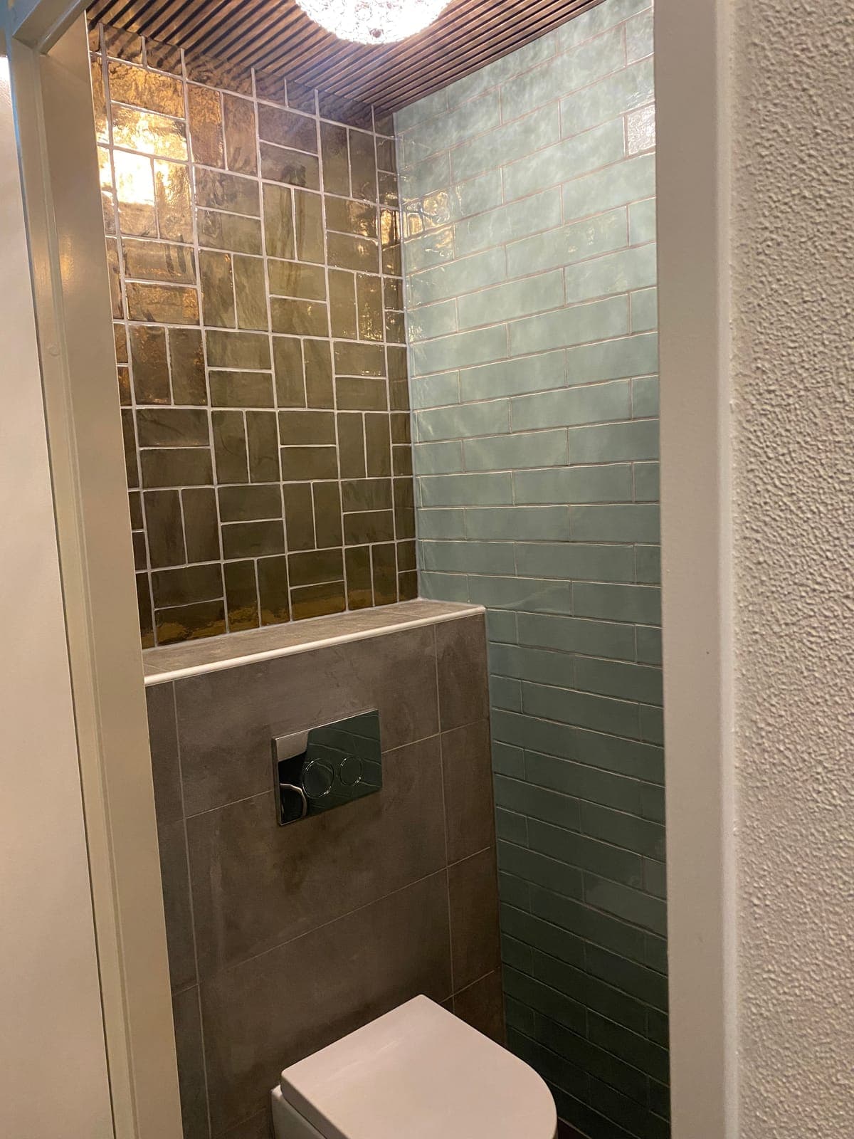 Vernieuwd toilet met petrolblauwe en bronzen tegels en houten lattenplafond